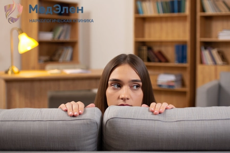 Девушка прячется за диваном